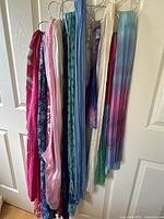 Set of colorful scarves hung on rings, showing a variety of colors and patterns including pink, blue floral, tie-dye and striped scarves.
