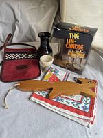 Photo showing red leather satchel with a geometric textile panel, wooden dog figure, ceramic vase, polished stone egg cup, boxed The Un-Candle glass candle holders, and colorful cloth beneath.