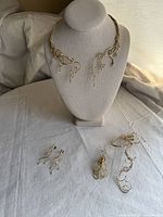 Gold tone artisan jewelry set displayed including choker necklace on bust stand, earrings, and bracelets laid out on fabric surface