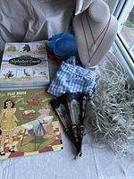 Overview of assorted fun items including paper dolls book, alphabet cards, necklaces on bust, small colorful plates, white string lights, fans, and fabric for scale and detail