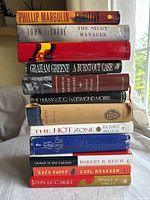 Stack of 12 books with visible titles and authors, showing varied book heights and colors against a neutral background.