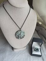 Necklace displayed on bust showing ceramic pendant with birds on branches design and matching ring in box.