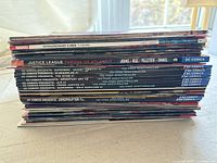 Stack of comic books showing DC Comics and Marvel titles including Extraordinary X-Men, Justice League, DC Comics Presents with Superman and others, arranged horizontally for scale and identification.