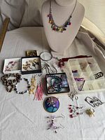 Overview photo showing entire assortment of colorful and varied jewelry including necklace, bracelets, earrings, and pins laid on a white cloth background.