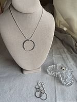 Photo of necklace on display stand with pendant visible, earrings placed on surface, and crystal dish with lid