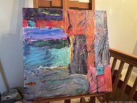 Full view of the mixed media abstract painting on canvas displayed on a wooden easel, showing vibrant, textured layers of paint and multiple bright colors.