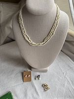 Full view of the necklace displayed on bust with three pairs of earrings arranged below, showing the overall lot items.
