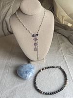 Necklaces and polished stone paperweight lot photo showing an amethyst necklace on a display bust, blue heart-shaped polished stone, and multi-colored bead necklace lying flat.