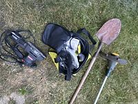Photo showing corded electric sander, protective goggles in carrying case, and rusty shovel on grass.