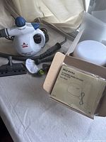 Photo showing Bissell SteamShot Deluxe handheld steam cleaner with accessories including multiple nozzles and microfiber pad, along with boxed Muji Ultrasonic Aroma Diffuser.