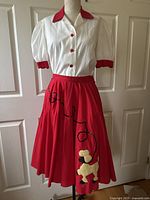 Full view of the vintage swing dance outfit on a dress form, showing white blouse with cherry red collar, buttons, and cuffs paired with cherry red circle skirt featuring black sequins and poodle applique