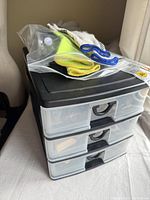 Three-drawer plastic tool storage unit with gloves and blue strap on top