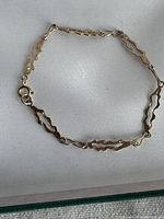 Photo of the entire gold bracelet laid flat on white fabric showing linked segments and clasp.