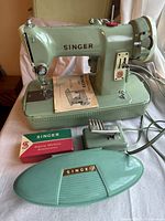 Front view of sewing machine atop its base, original manual, attachments box, buttonholer box, and case lid