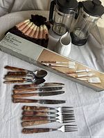 Overview photo of the BBQ utensil set laid out with tea cozy, French presses, and creamer pitcher. Shows the boxed BBQ set and rosewood-handled forks, knives, and spoons.
