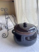 Photo showing black glazed bean pot with lid and black metal cookbook stand in background