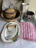 Full lot including woven baskets, ceramic vases, metal watering can, ceramic plates, cloth napkins, and mezzaluna chopper on table