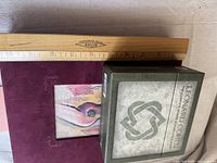 Top-down view of Leonard Cohen green box next to a wooden ruler, showing approximate size (about 6 inches).