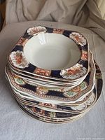 Stack of vintage square dishes and bowls with ornate floral decoration in rust, navy, gold and white glaze.
