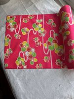 Rolled pink fabric with multicolor floral pattern laid on white surface, showing the pattern and partial length.