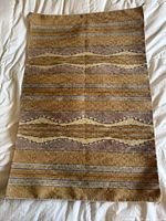 Full view of the Navajo rug laid flat on a white background showing the entire woven piece with natural striped geometric patterns in earth tones.