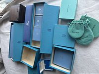 Assorted open and closed Tiffany blue jewelry boxes and turquoise pouches arranged on fabric surface