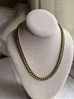 Front view of the thick gold tone curb chain necklace displayed on a necklace stand.