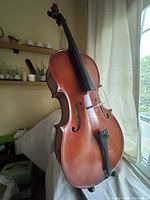 Full view of cello standing upright against curtain