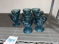 Eight blue glass dessert cups arranged in two rows on a metal shelf, showing the full set.