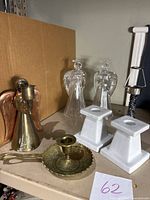 Photo showing all candlestick holders: two brass with copper-colored wings, two crystal angel Avon holders, two white ceramic square holders, and one brass votive holder missing shade.
