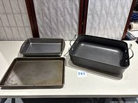 Roasting pan with handles, two baking pans, and baking sheet on white table.