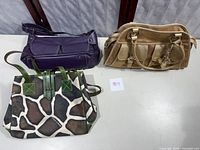 Three assorted handbags: purple, gold, and canvas animal print displayed on a chair.