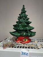 Full view showing entire green ceramic Christmas tree with red base and bundled multicolored bulbs with cord.