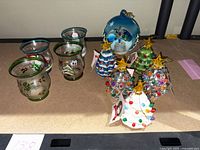 Four hand painted glass candle holders with Christmas designs alongside several Mr. Christmas battery operated Christmas tree ornaments and one large spherical ornament.