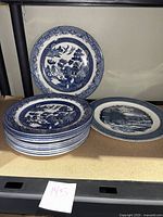 10 Churchill Willow pattern plates stacked and Currier and Ives platter next to them on shelf.