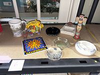 Multiple collectible items displayed on table including ashtrays, piggy bank, tile, mug, shot glass, totem, and paperweight