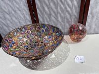 Large decorative metal bowl with multicolored stones alongside multicolored hand blown glass ball