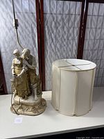 Porcelain lamp base with Dutch man and woman figurine next to the fabric lampshade, showing overall lamp components.