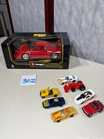 Photo showing the 1987 Bburago Ferrari F40 die cast model in original black and yellow packaging alongside 7 small toy cars in varying colors and styles.