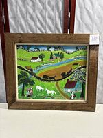 Framed folk art painting in a rustic wooden frame showing a rural landscape with houses, horses, and people.