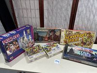 Photo showing six boxed items including Monopoly Star Wars game, Scavenger Hunt, Hangman, 3D puzzle castle, and two 500-piece jigsaw puzzles arranged on a table.