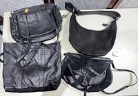 Four assorted handbags placed on a table including three black leather bags and one small black fabric bag.