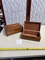 Two wooden jewelry boxes on a beige surface, one open showing interior with mirror and Cedar Chest branding, the other closed with visible brass accents.