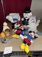 Wide view of all items in the lot arranged on table including Mickey Mouse mini bean bag toys, Abominable Snowman and Sam the Snowman figures, vintage ceramic figurines, Winnie the Pooh mug and spoon.