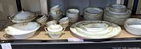 Wide view of full Noritake dinnerware set on shelf showing platters, plates, bowls, sugar bowl, covered dishes, tea cups with saucers
