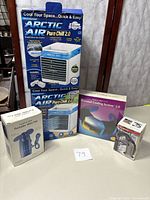 Full view of all cooling devices including Arctic Air boxes, Sharper Image box, and two smaller mini fan boxes