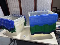 Six translucent plastic storage boxes with blue, green, and navy attached lids stacked and open.