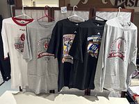 Photo showing five assorted Boston Red Sox World Series t-shirts in size XXL hanging on hangers, featuring various championship logos and years.