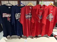 Five XXL Red Sox World Series and division championship T-shirts hanging, showing front graphics for multiple years and titles.