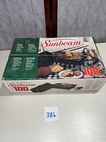 Box of Sunbeam 100 Portable Glass Grill with branding and food displayed on grill.